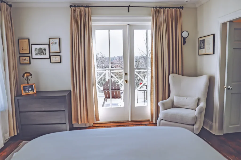 A boutique guest room at Hotel Fauchère featuring a wingback chair and balcony doors overlooking Milford, PA.