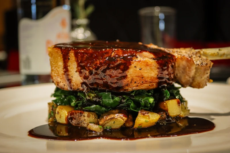 A glazed bone-in chop over greens and potatoes, showcasing refined Milford PA dining at the Delmonico Room.