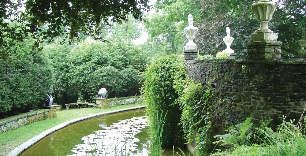 Lily pads float on a peaceful pond surrounded by stone walls and greenery in the historic Hotel Fauchère gardens.
