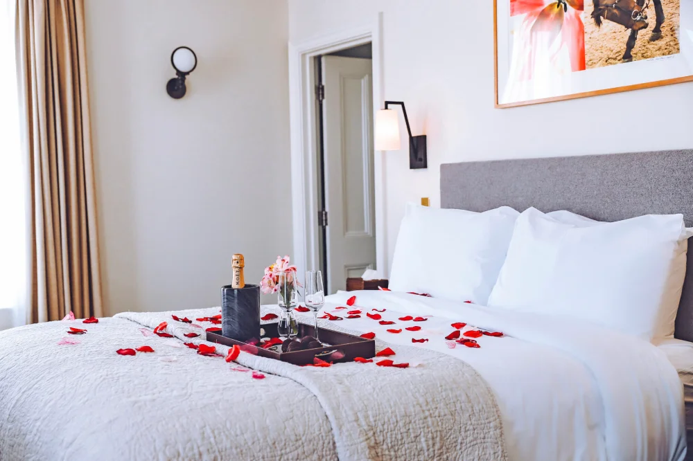 Red rose petals and a champagne tray rest on a bed for a romantic stay at Hotel Fauchère in Milford PA.