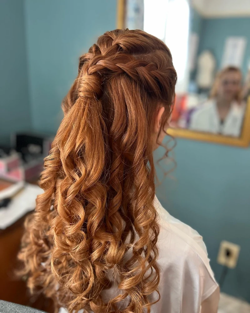A woman with cascading auburn curls and an intricate braid prepares for a special day at our Milford wedding venue.