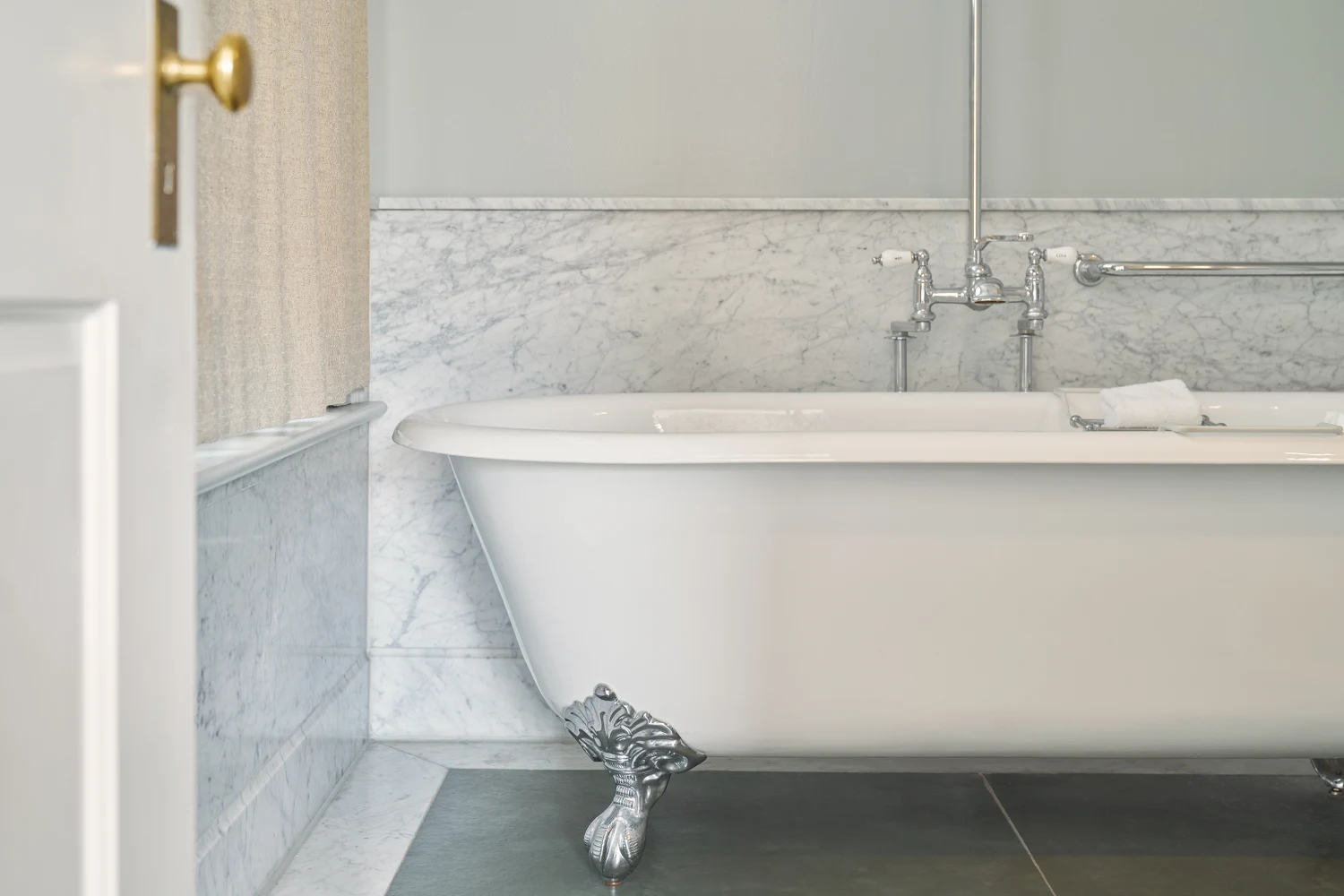 A classic white clawfoot soaking tub sits against a marble wall in a luxury suite at Hotel Fauchère.