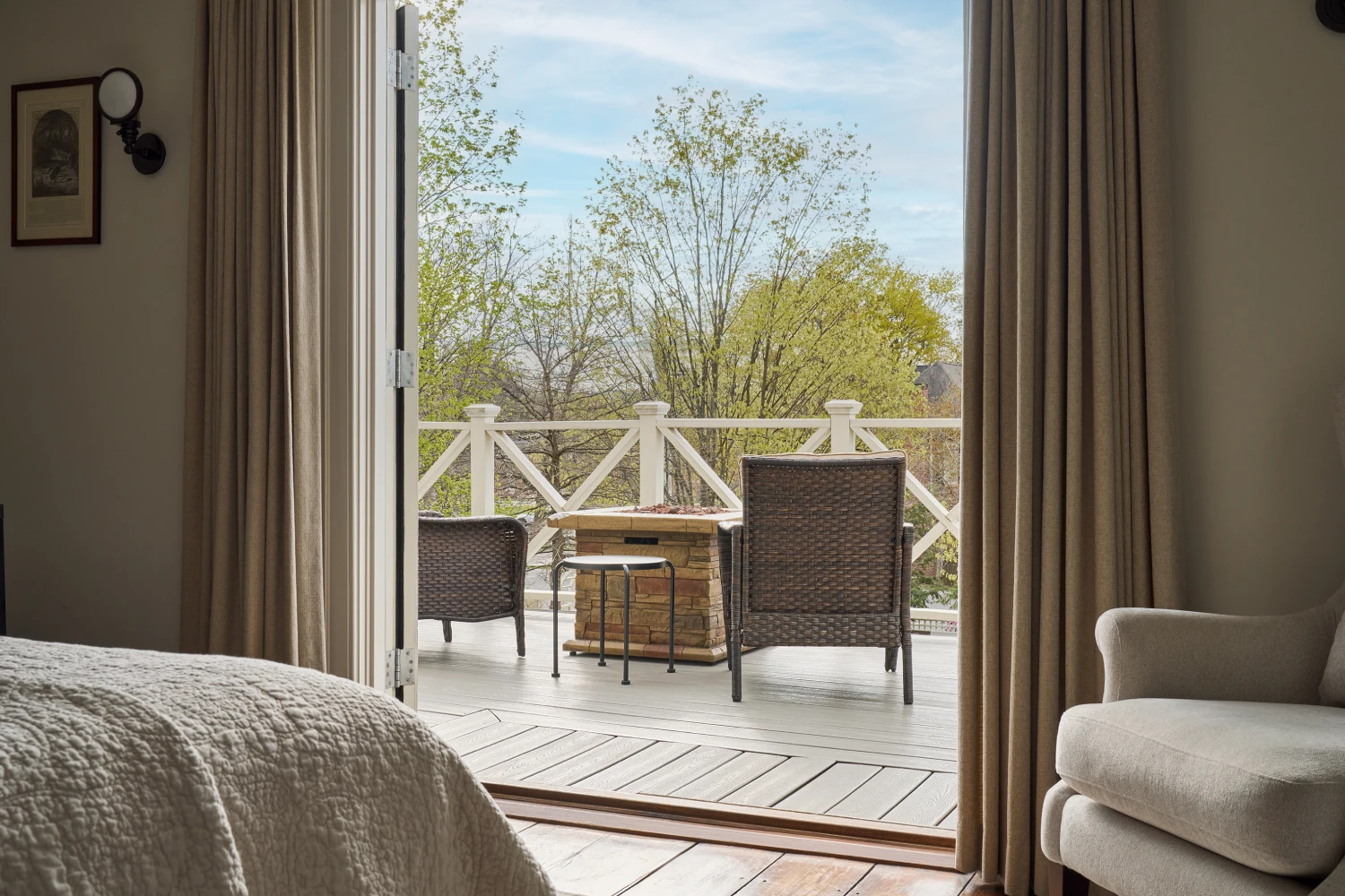 Wicker chairs and a fire pit table sit on a private balcony overlooking trees at a Milford, PA hotel.