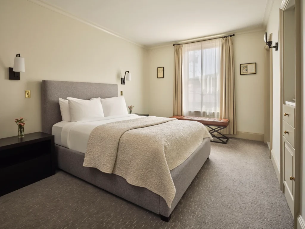 A bright, elegant guest room features a plush grey bed and neutral decor for a relaxing stay in Milford.