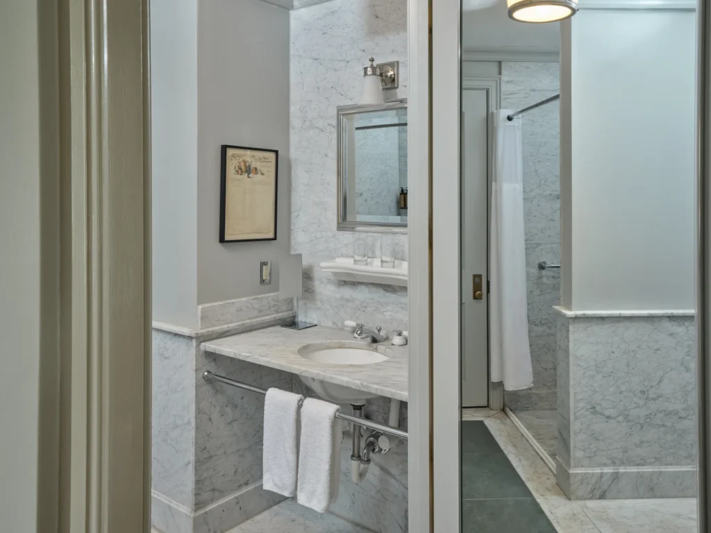 A bright marble bathroom with a vanity sink and shower, offering luxury places to stay in Milford, PA.