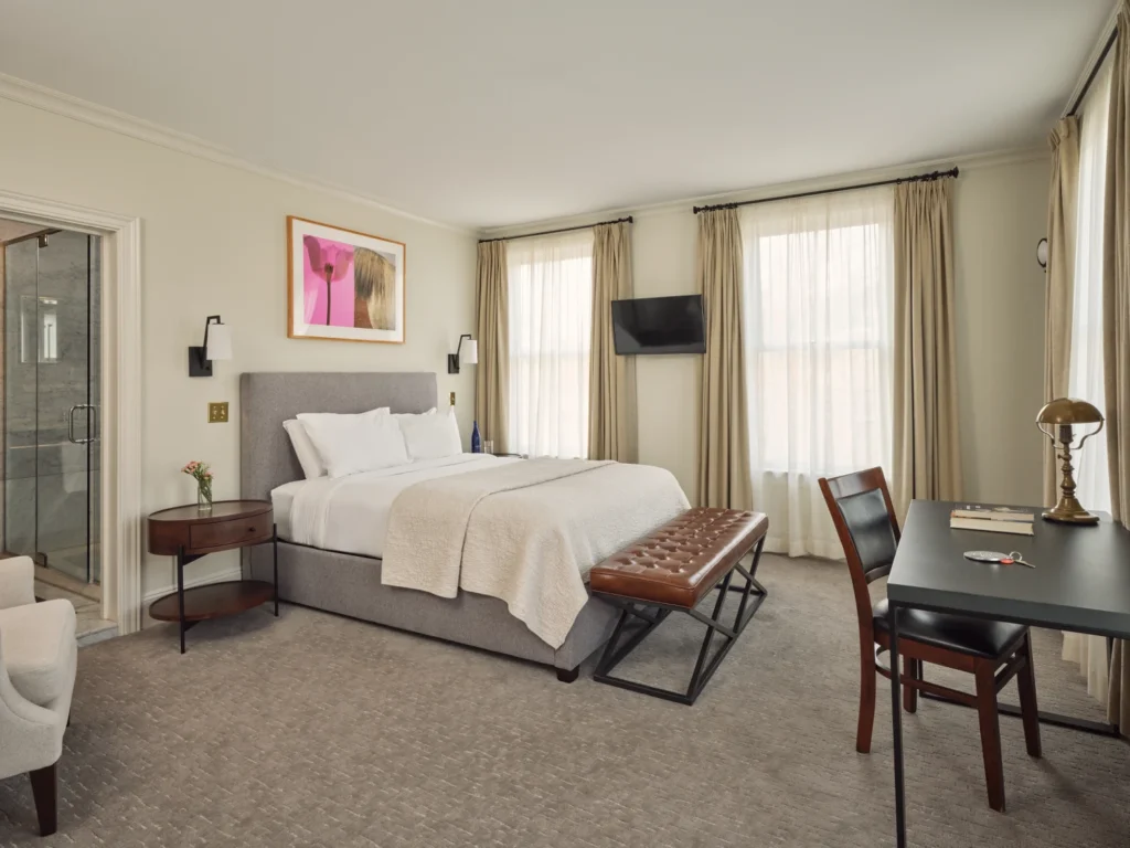 A bright guest room at Hotel Fauchère featuring a king bed, leather bench, and workspace in Milford, PA.