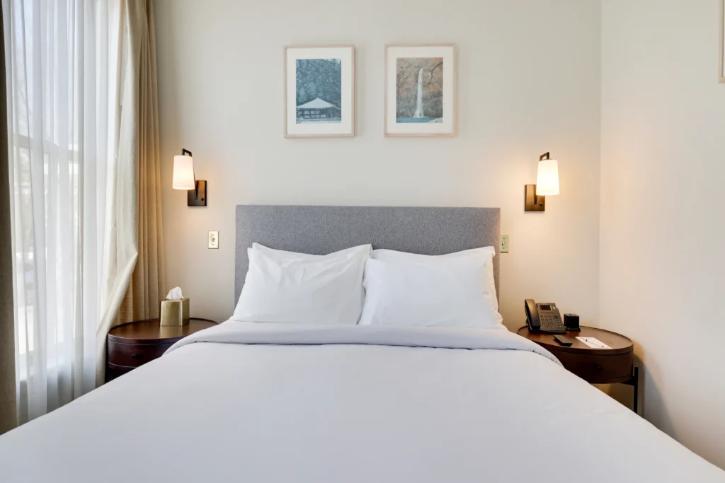 A bright guest room at Hotel Fauchère featuring a plush bed, grey headboard, and minimalist bedside lamps.