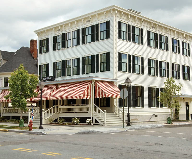 The grand exterior of Hotel Fauchère features classic black shutters and striped awnings in Milford, PA.