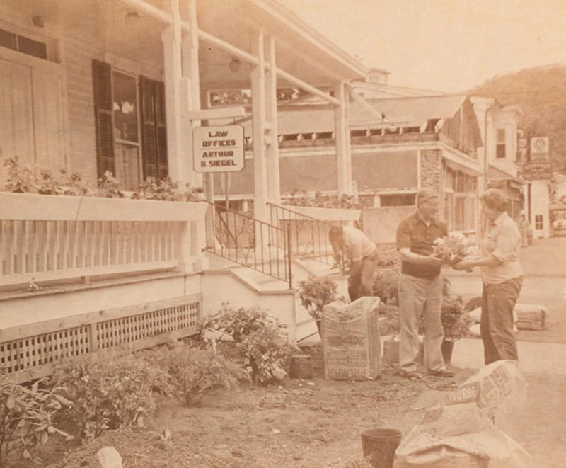 A nostalgic sepia photo of locals gardening near a law office within the Milford historic district.