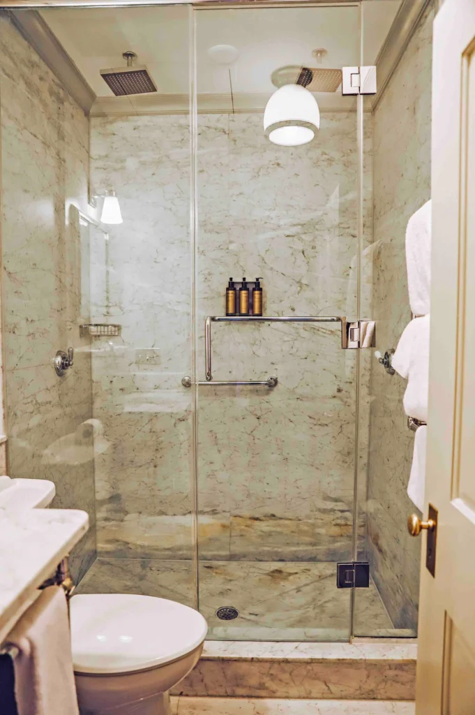 A luxurious walk-in marble shower with a glass door and rain shower head in a Milford PA accommodation.