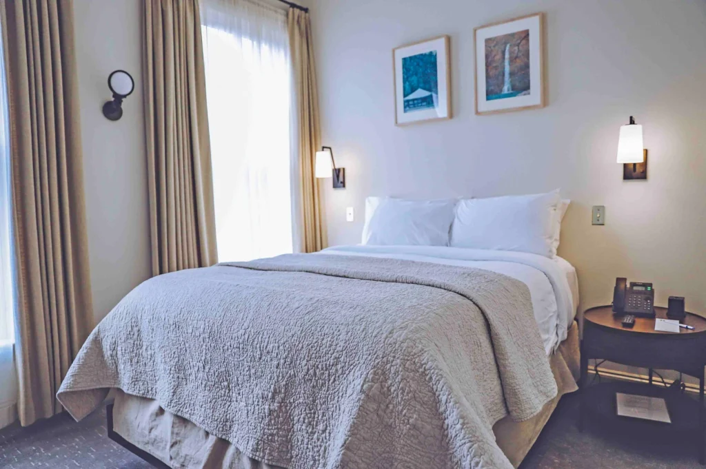 A bright guest room in Milford PA featuring a queen bed with plush white pillows and a textured beige coverlet.